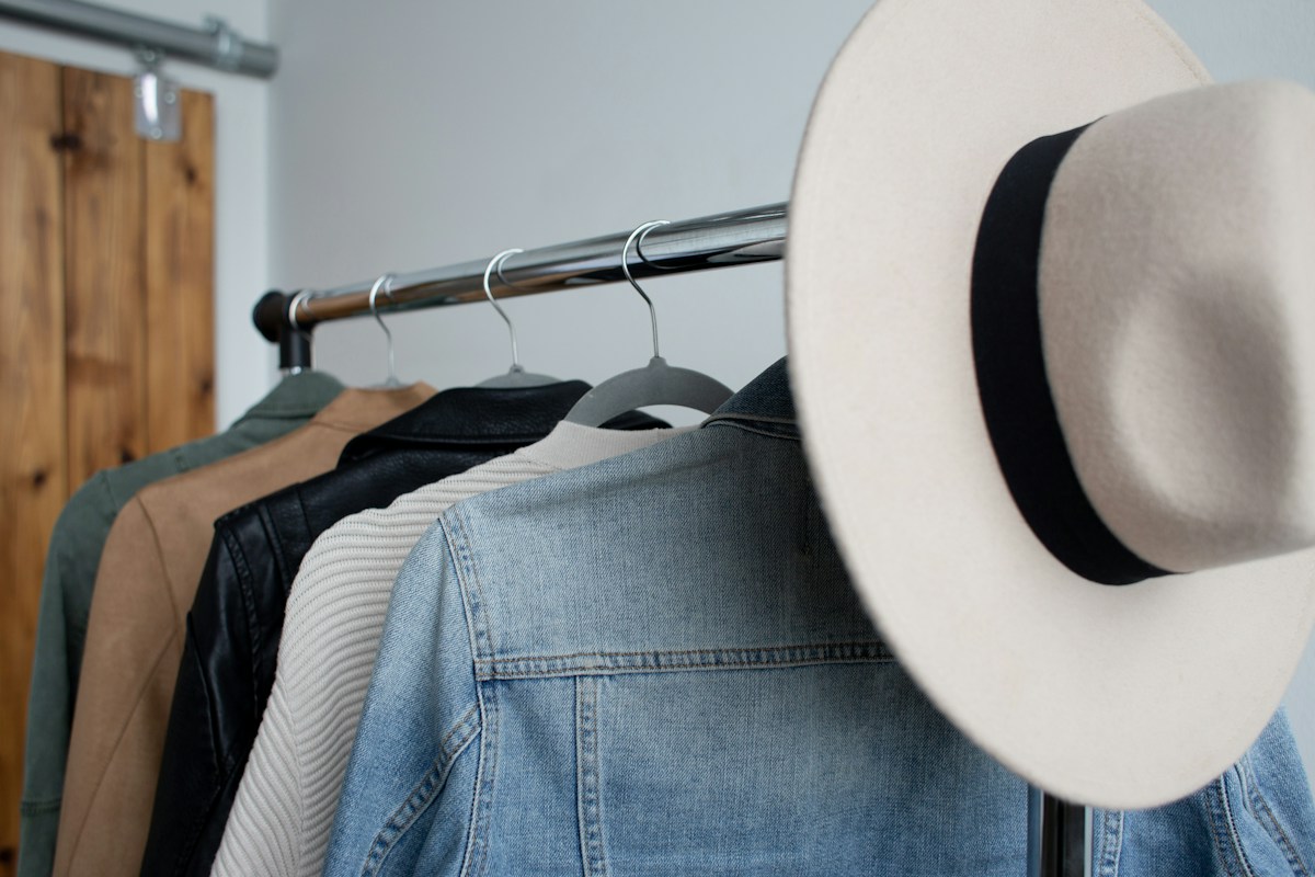 Denim, jackets, and a hat on a clothing rail — representative stock photograph